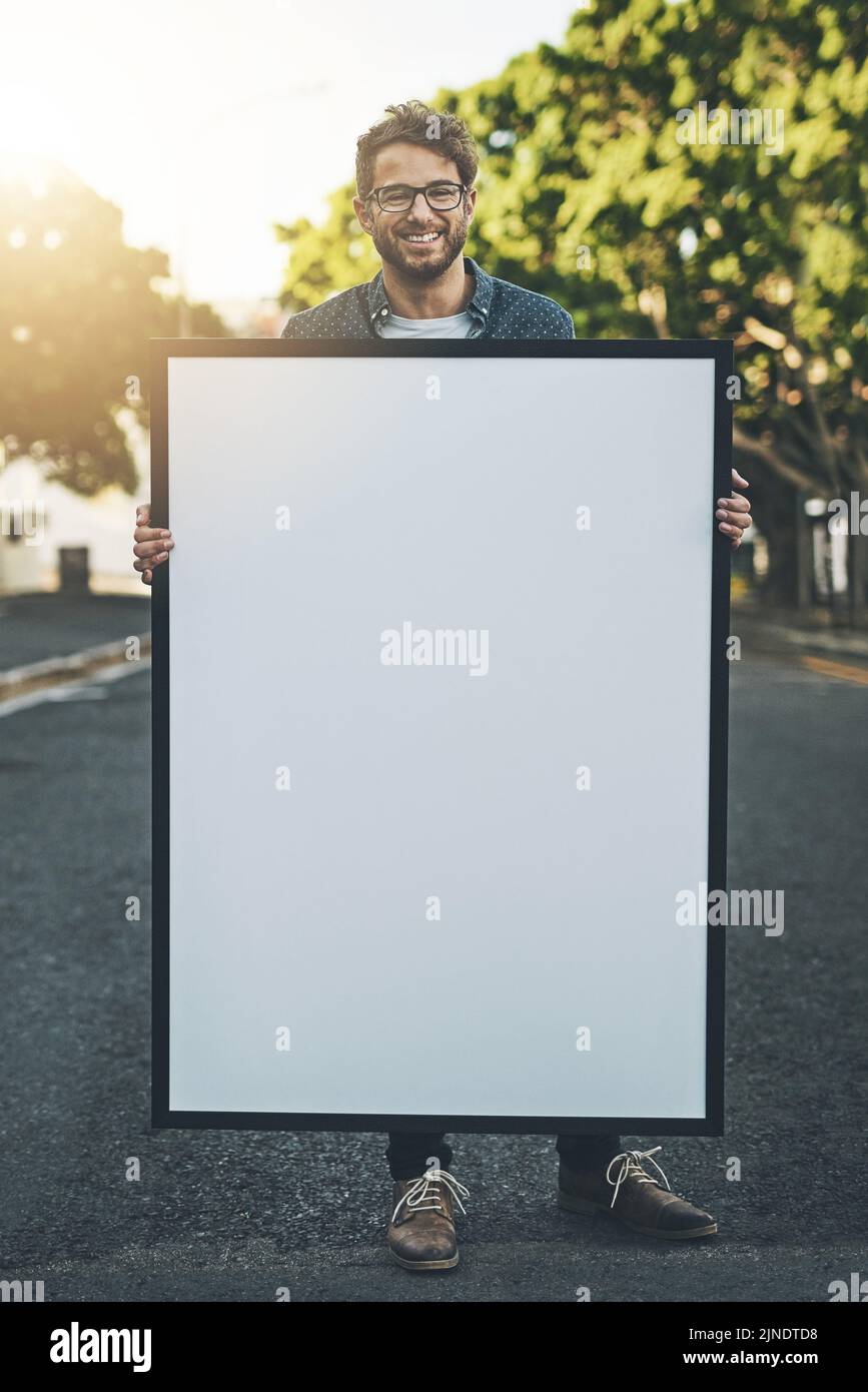 Glücklicher junger Mann, der im Freien ein Plakat mit einem Kopierraum hält. Lächelnder Typ mit einem großen Plakat oder Schild für Message Design, Werbung und Marketing für Stockfoto