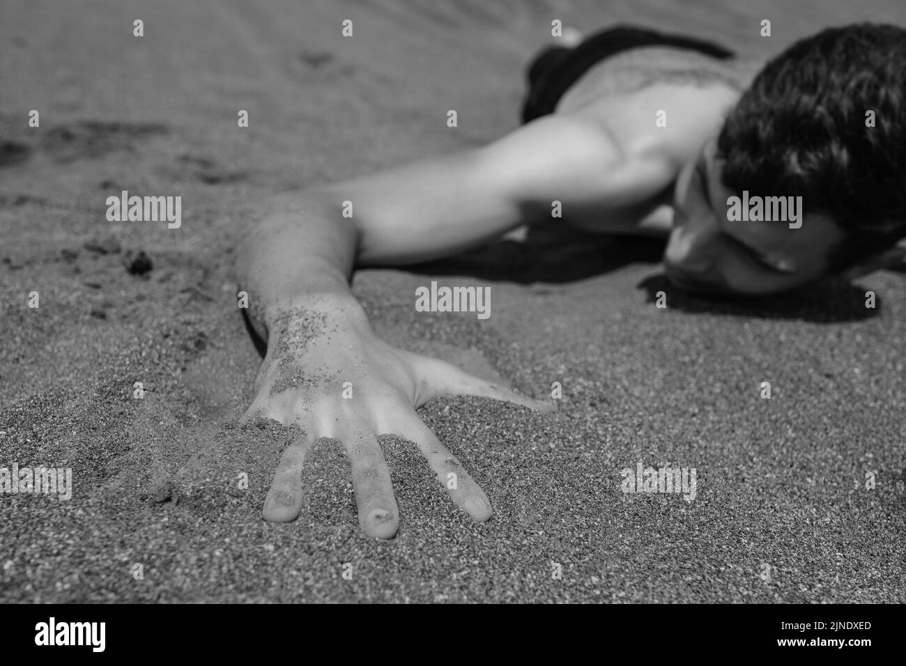 Mann liegt auf dem Bauch auf Sand in der Wüste. Selektiver Fokus auf die Hand im Vordergrund Stockfoto