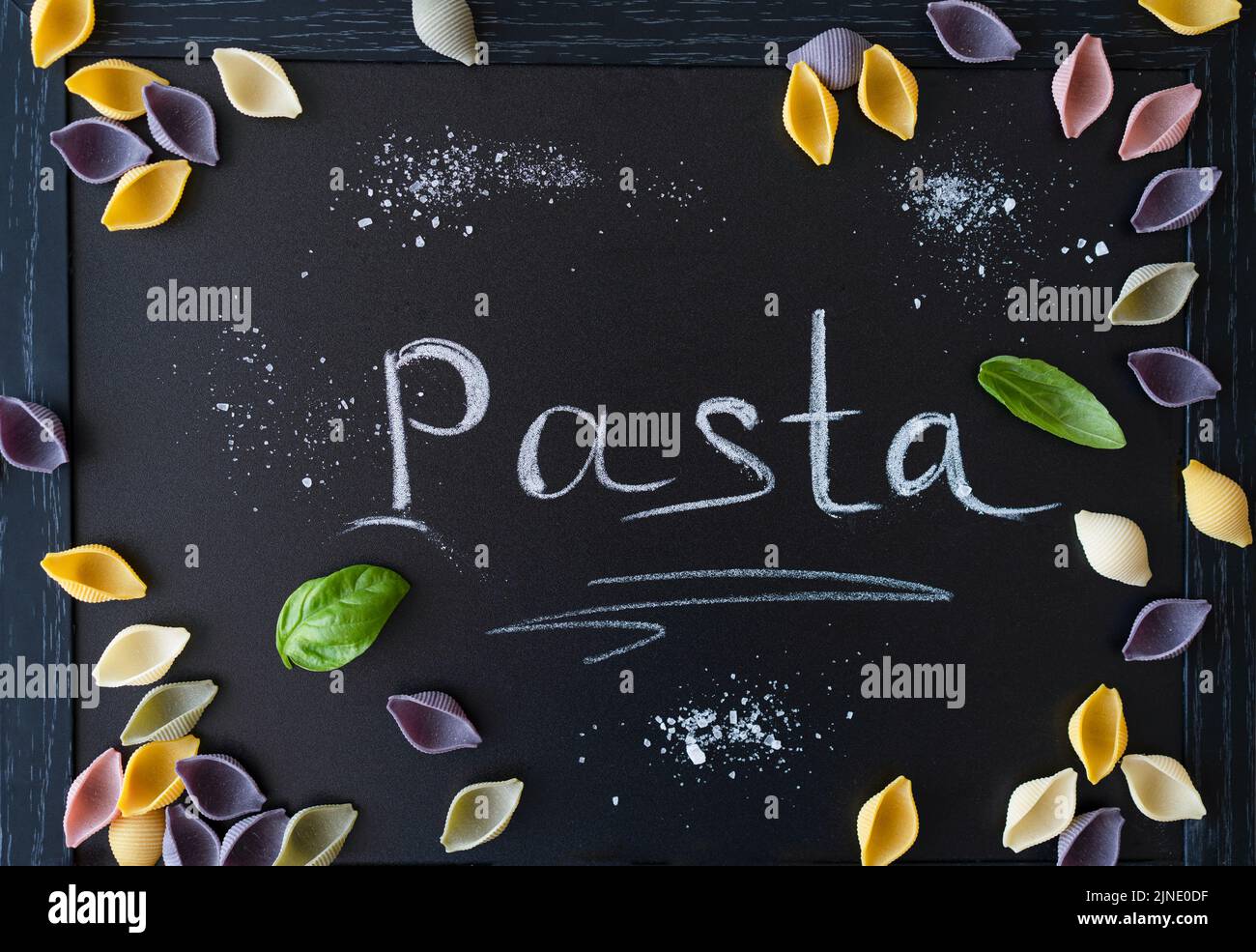 Mehrfarbige italienische Pasta-Conchiglie oder Muscheln mit Basilikumblättern auf Kreidetafel. Wort Pasta schrieb mit Kreide Stockfoto