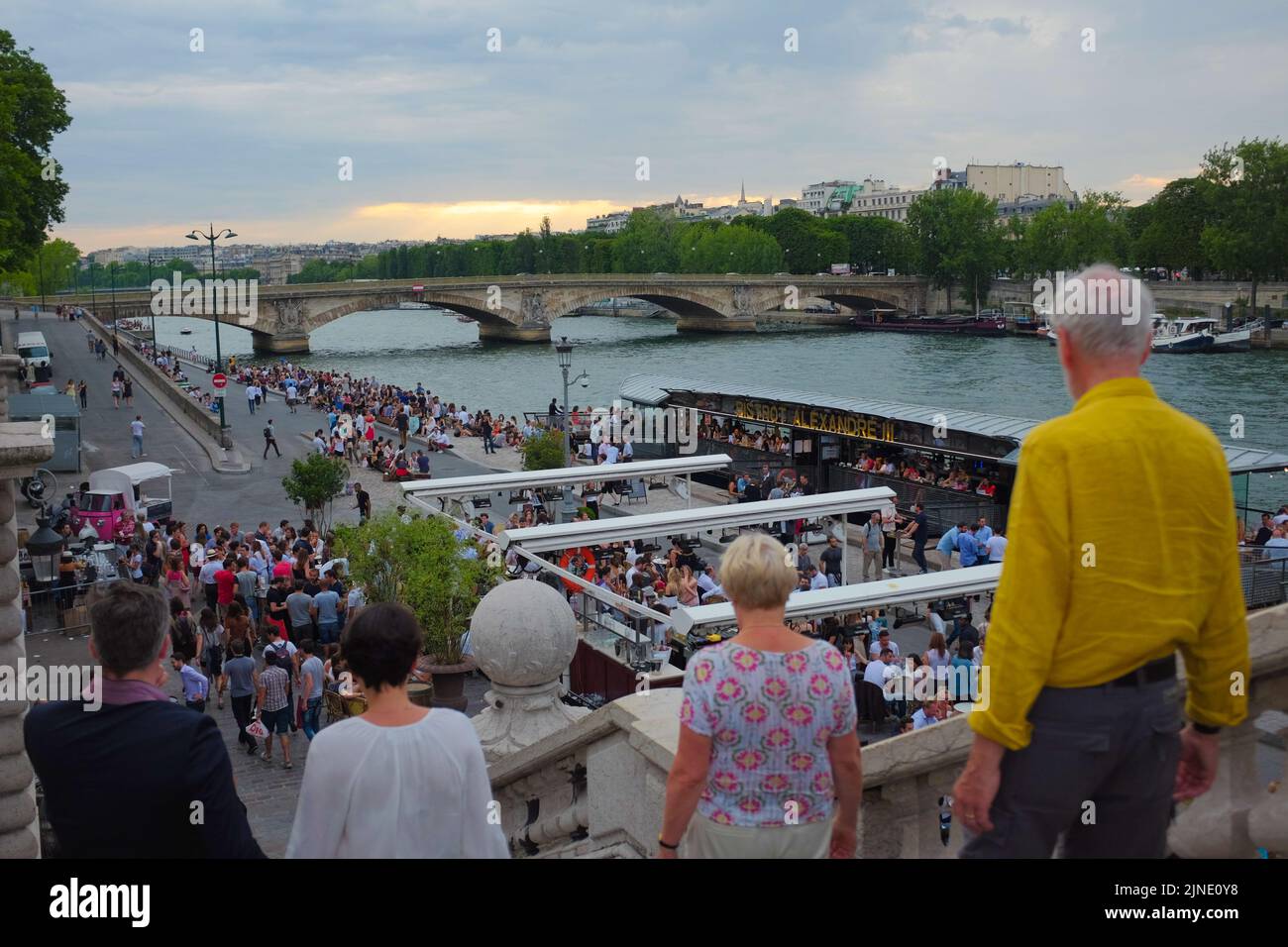 Zwei Paare gehen die Stufen hinunter, um sich der riesigen Menschenmenge anzuschließen, die an der seine hängt. Schöner Sommertag im Freien in Paris, Frankreich. Stockfoto
