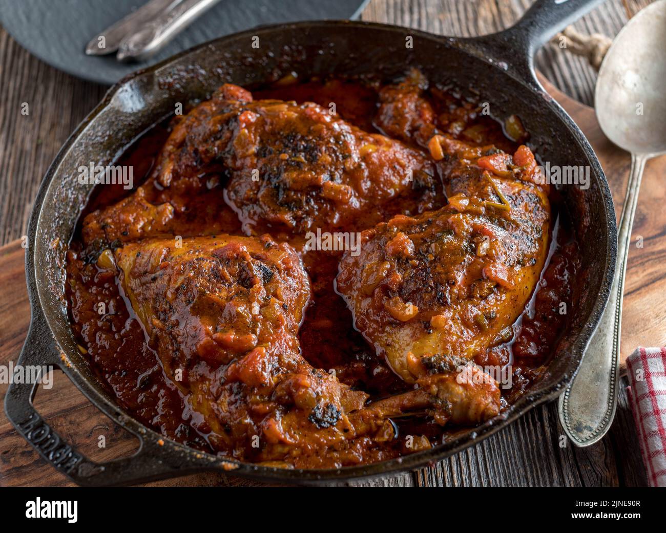 Geschmorte Hähnchenschenkel mit italienischer Tomatensoße in einer rustikalen Gusseisenpfanne auf einem Holztisch Stockfoto