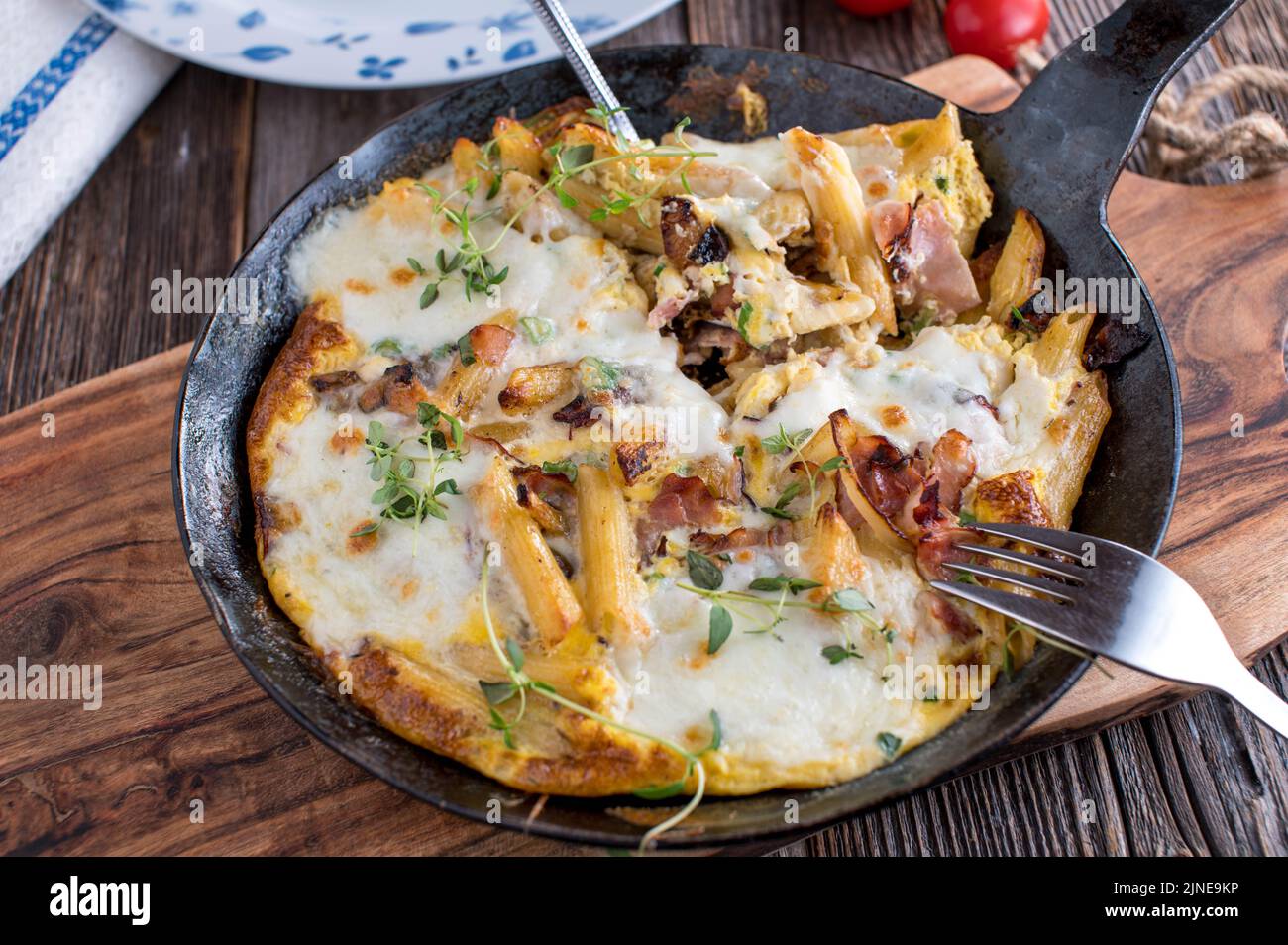 Gebratene Pasta mit Rührei, roten Zwiebeln, Schinken und Mozzarella-Käse in einer Pfanne Stockfoto