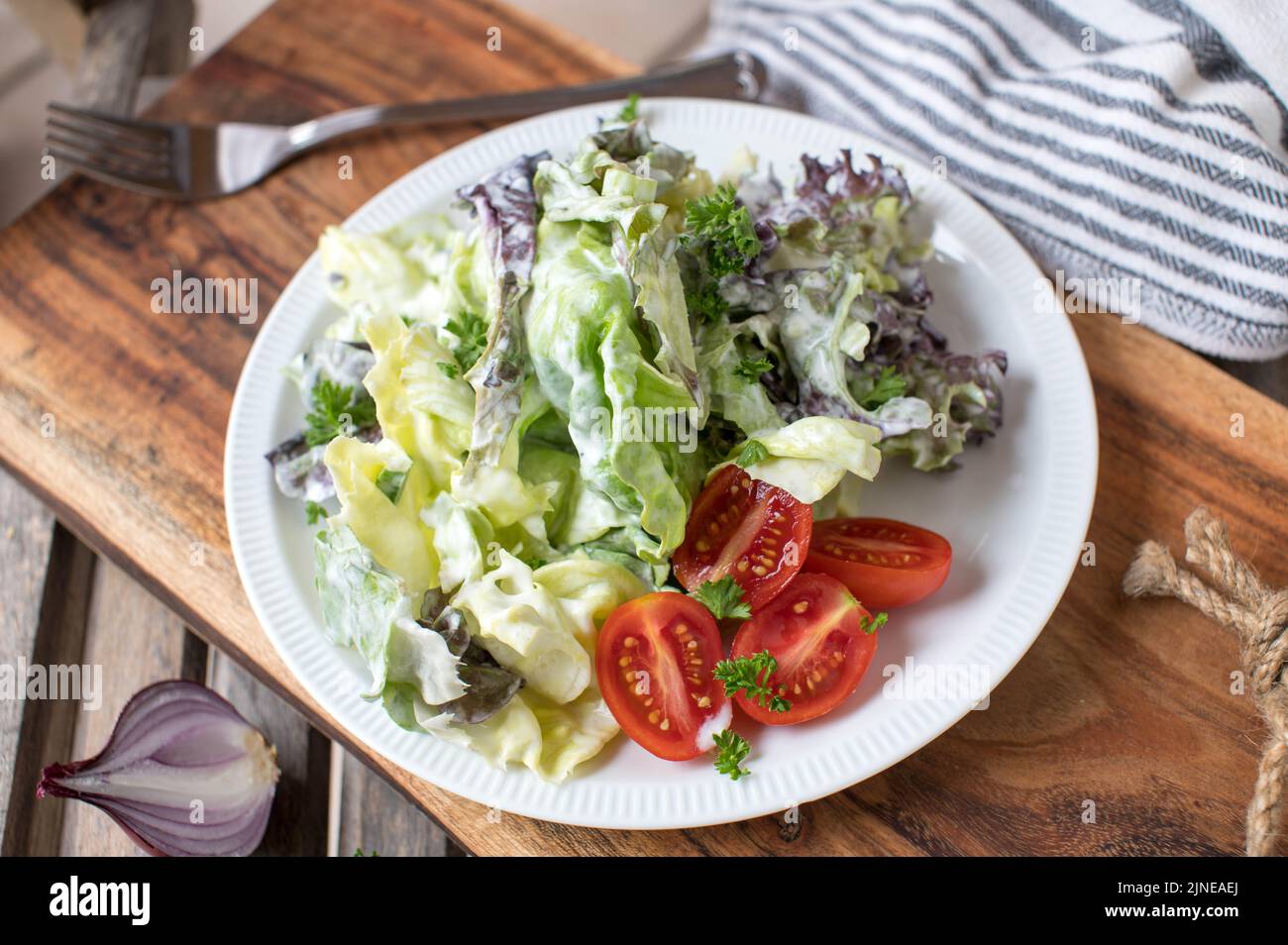 Beilagensalat mit Salat und Tomaten auf einem mit Sauerrahm-Dressing marinierten Teller. Traditionelle deutsche Beilage oder Vorspeise Stockfoto