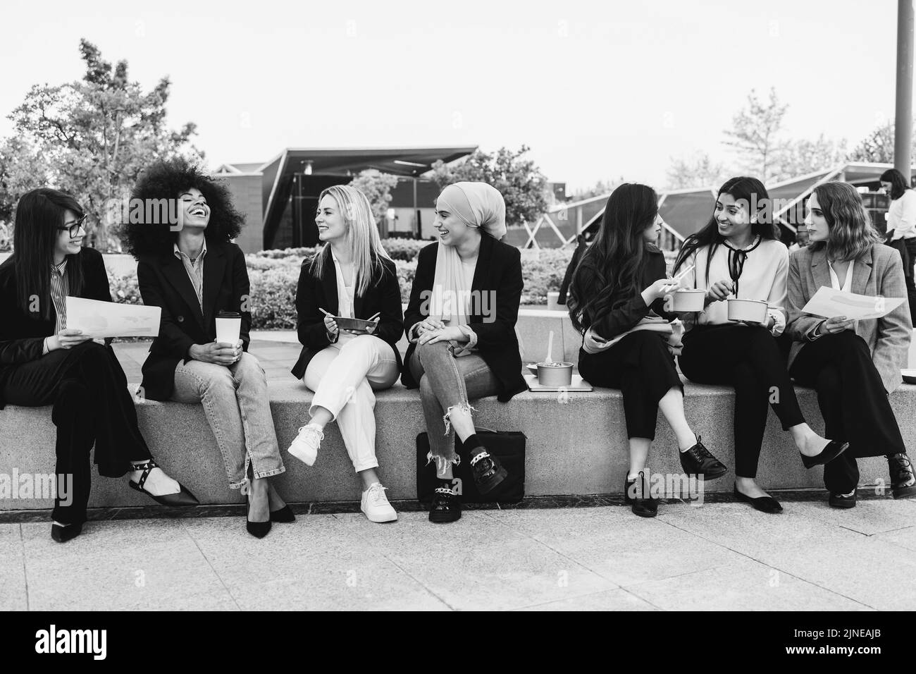 Multiethnische Geschäftsfrauen machen Mittagspause im Freien aus dem Bürogebäude - Fokus auf blondes Mädchengesicht - Schwarz-Weiß-Schnitt Stockfoto