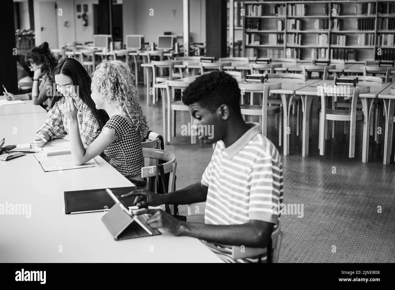 Junge multiethnische Gruppe von Studenten, die in der Universitätsbibliothek studieren - Fokus auf linkes Mädchengesicht - Schwarz-Weiß-Schnitt Stockfoto