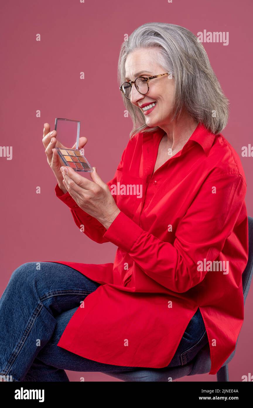 Reife Frau mit Lidschatten in den Händen und lächelnd Stockfoto