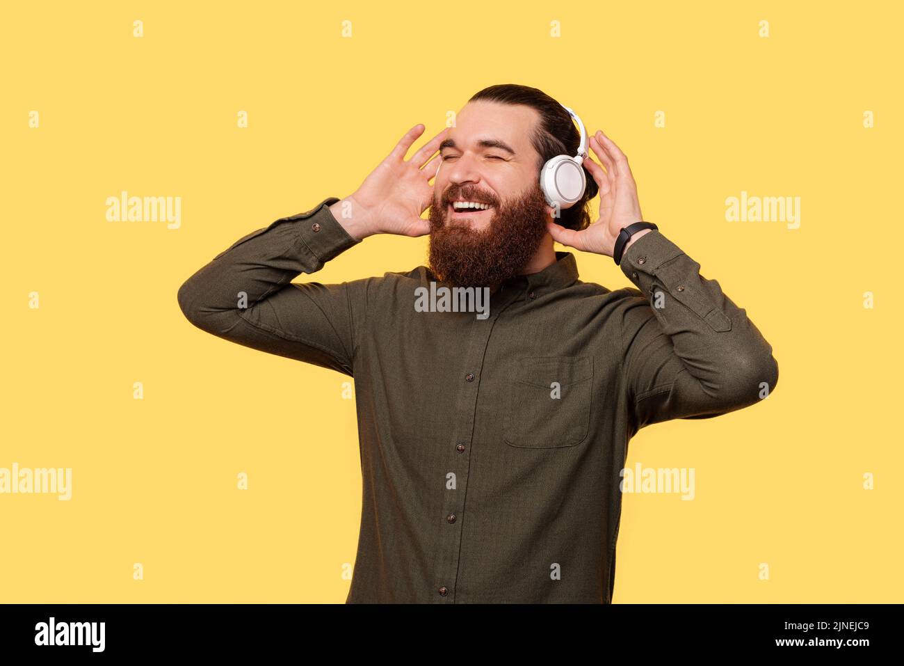 Ein bärtiger Mann genießt freudig die Musik, die er über seine neuen Kopfhörer hört Stockfoto