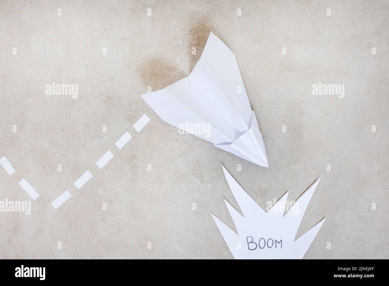 Papierflugzeug als Metapher, auf einen Absturz oder eine Explosion zusteuend, auf grau mit Kopierraum Stockfoto