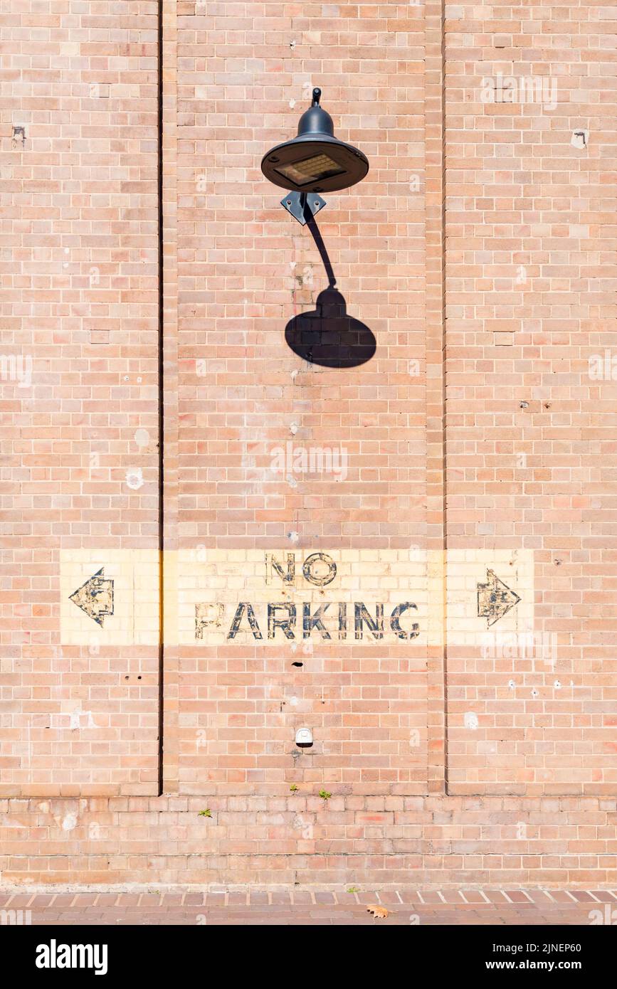 Eine hohe Backsteinmauer mit einem LED-Flutlicht im antiken Stil und einem alten No Parking-Schild am National Innovation Center in South Eveleigh, Sydney Stockfoto
