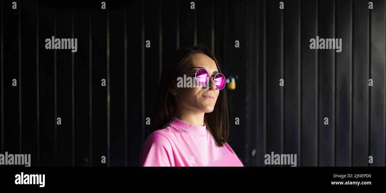 Junge Erwachsene lächelnde Frau in rosa sitzt in einem Rollstuhl mit Sonnenbrille Stockfoto