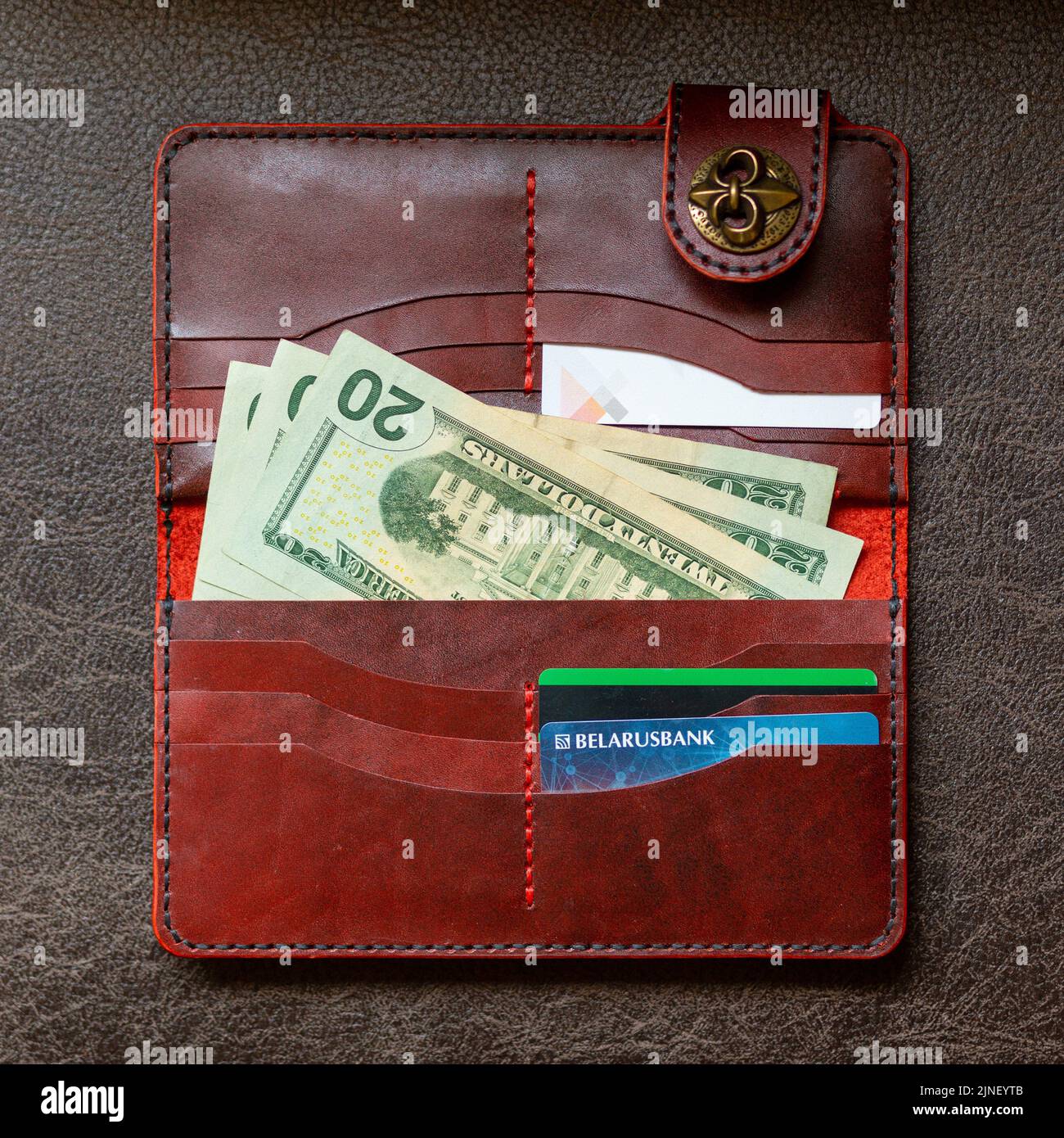 Offene rote Lederkupplung mit Geld und Kreditkarten auf braunem Lederhintergrund. Stockfoto