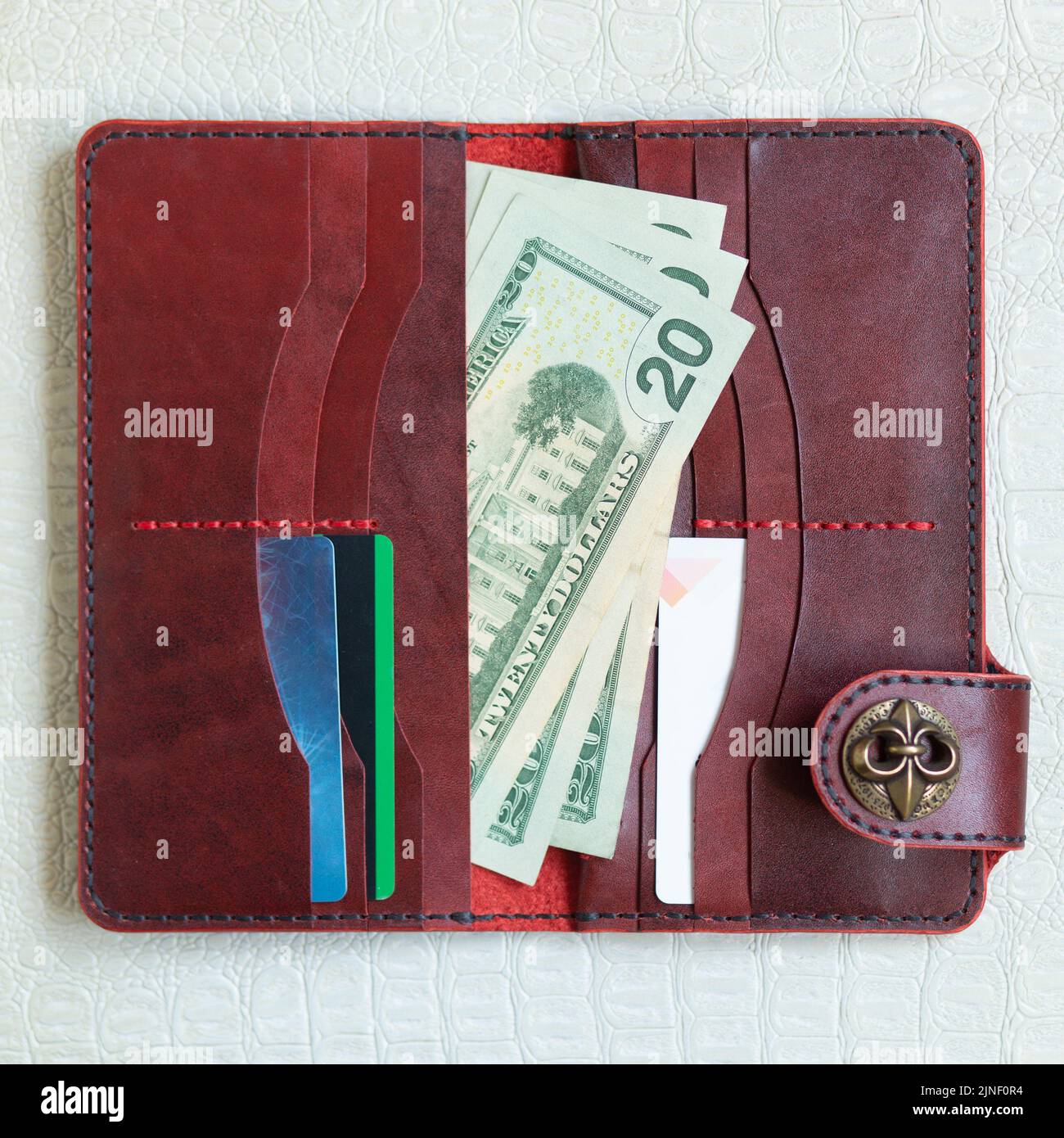 Offene rote Lederkupplung mit Geld und Kreditkarten auf hellem Lederhintergrund. Stockfoto
