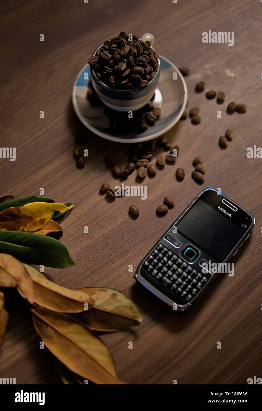 Das alte Handy Nokia E72, Kaffeebohnen und trockene Blätter auf einem Holztisch Stockfoto
