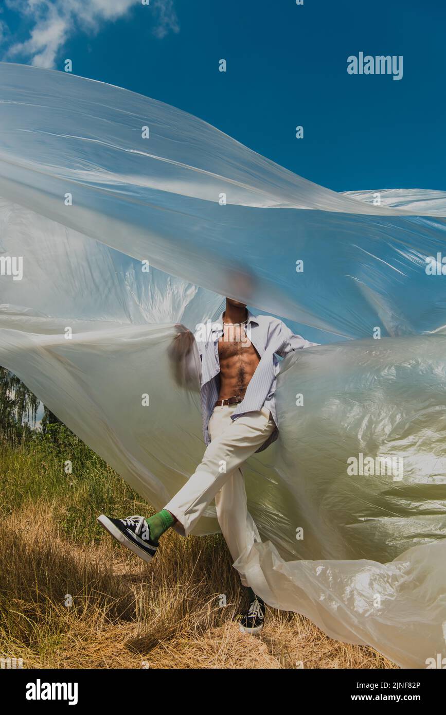 afroamerikanischer Mann in weißen Hosen, posiert unter Polyethylen auf dem Feld, Stockbild Stockfoto