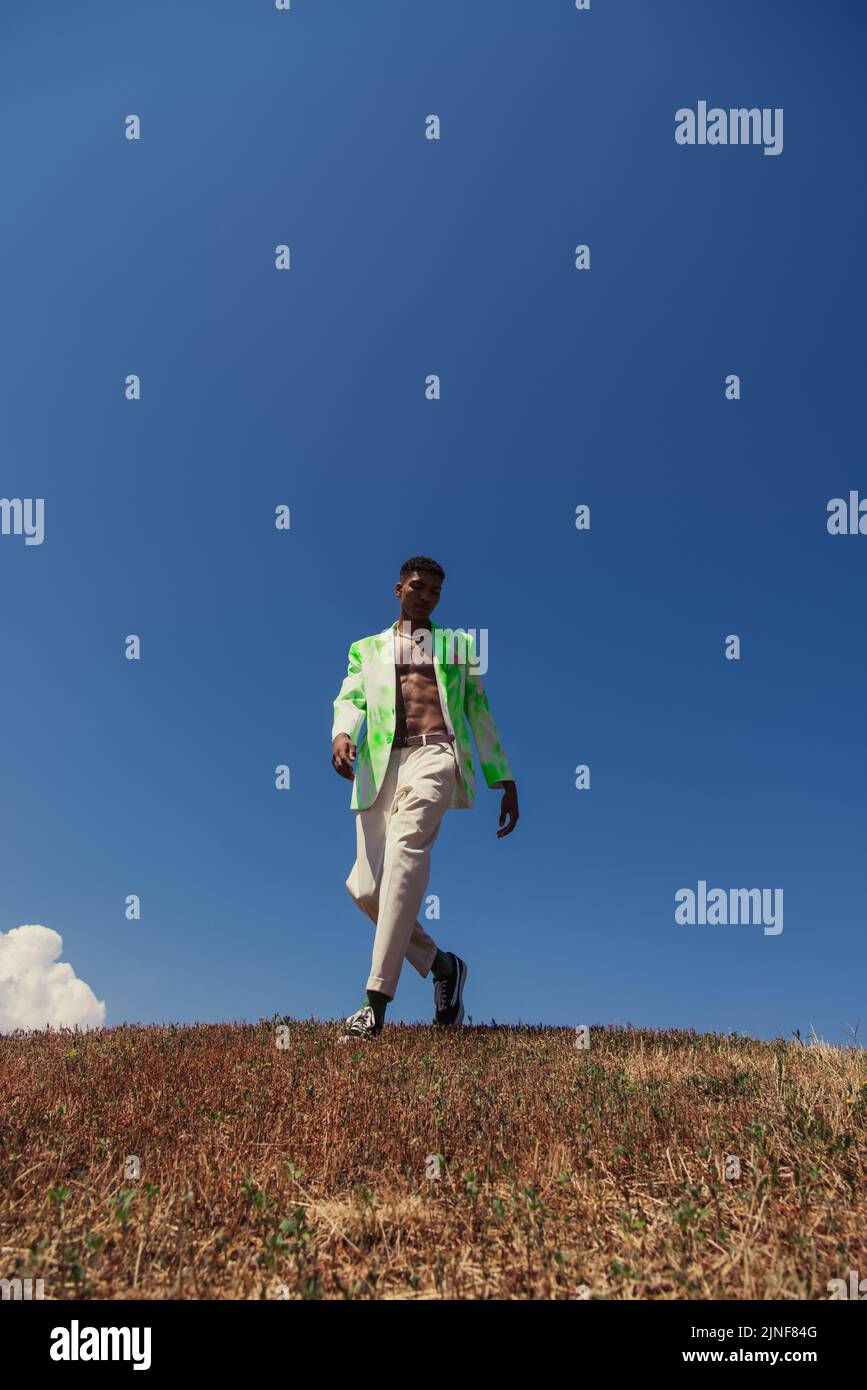 Volle Länge der modischen afroamerikanischen Mann zu Fuß im Feld gegen blauen Himmel, Stockbild Stockfoto