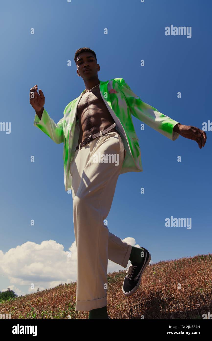 Low-Angle-Ansicht des afroamerikanischen Mannes in weißen Hosen und Blazer gegen blauen Himmel, Stockbild Stockfoto