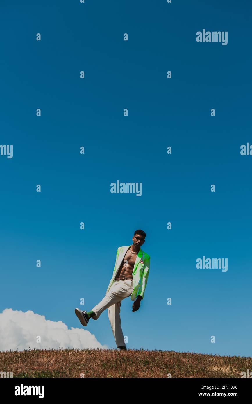 In voller Länge afroamerikanischer Mann in weißer Hose und Blazer unter blauem Himmel im Feld, Stockbild Stockfoto