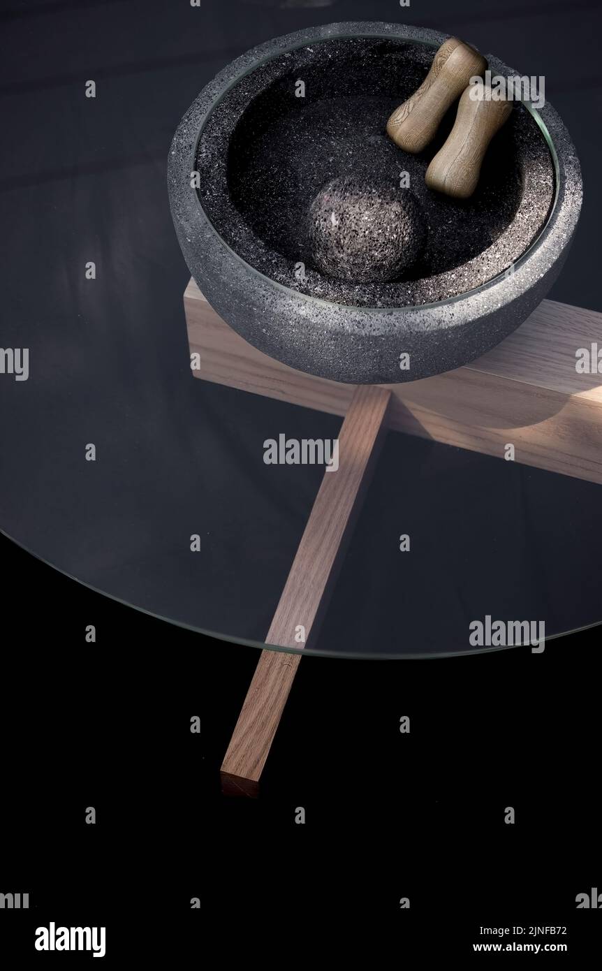 Eine vertikale Aufnahme einer schwarzen Granitkugel in einer schwarzen Schüssel mit Holzstäben zum Rühren, platziert auf einem Tischglas, ideal für die Inneneinrichtung Stockfoto