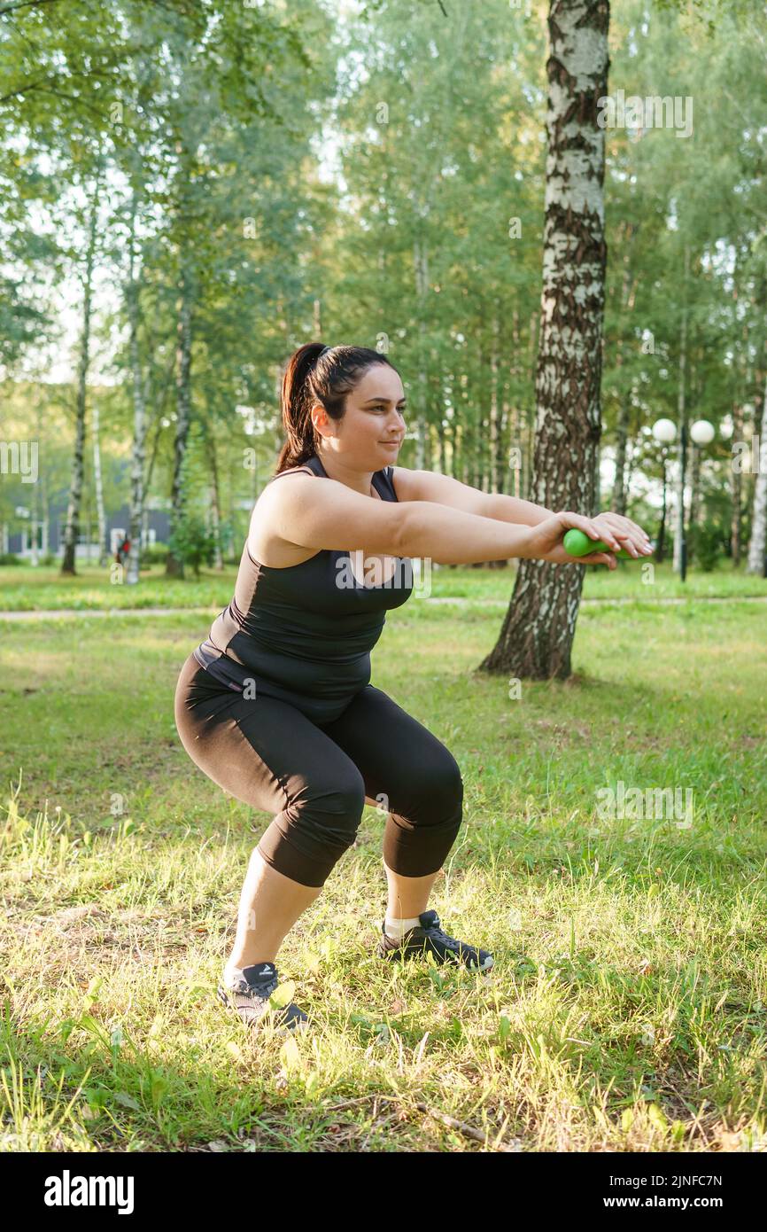 Eine charmante Brünette Frau plus-Größe Körper positiv praktiziert Sport in der Natur. Übungen mit Kurzhanteln. Stockfoto