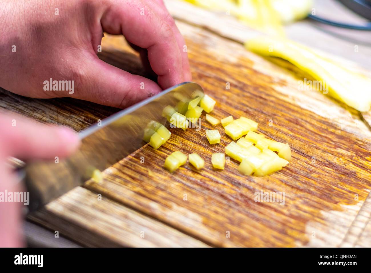 Detail von gehacktem Pfeffer. Silbernes Messer mit Händen. Gesundes Gemüse auf Holztisch gestellt. Stockfoto