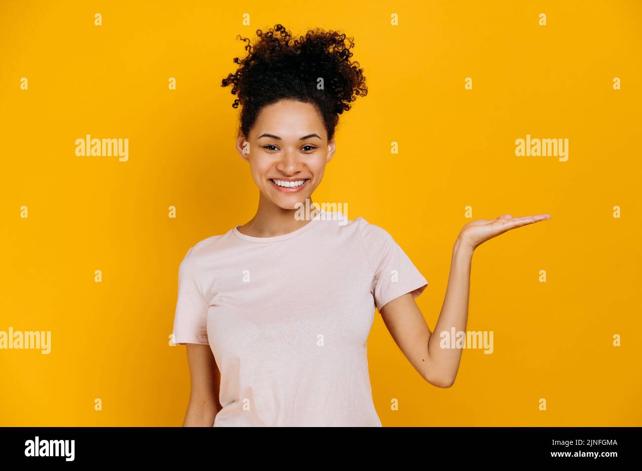 Foto einer freundlichen afroamerikanischen jungen Frau im lässigen T-Shirt, blickt auf die Kamera und zeigt die Hand zur Seite, auf leeren Raum für Präsentation oder Text, steht auf isoliertem blauen Hintergrund, lächelt Stockfoto