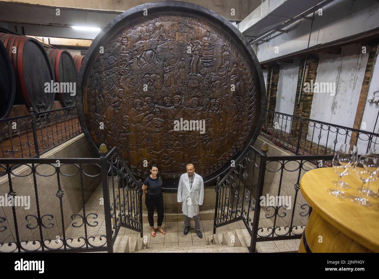 Am 11. August 2022 Mitglied des Vorstands von Erdut Vineyards Dunja Vukmirovic und Chief Oenologist Damir Risek vor dem Big Barrel of Erdut Vineyards in Erdut, Kroatien. Das Big Barrel of Erdut Vineyards ist das größte in der Welt verwendete Weinfass. Sein Fassungsvermögen beträgt 75.000 Liter, das sind 100.000 Flaschen Wein. Das Fass ist mit zweieinhalb Tonnen Fesseln verkettet, mit kroatischen Korbreliefs verziert, sowie mit dem Letzten Abendmahl, wo Jesus einen Kelch Wein hält, und wurde von den naiven Bildhauern Tijardovic und Fodor dekoriert. Es besteht aus 150 Jahre alter slawonischer Eiche, und Stockfoto