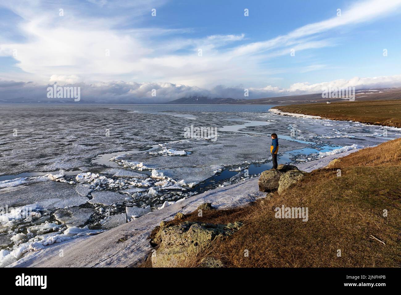 Ein Junge, der den gefrorenen Paravani-See und die schneebedeckten Berge im Hintergrund beim Sonnenuntergang ansieht, das Vulkanplateau Javakheti, Georgia Stockfoto