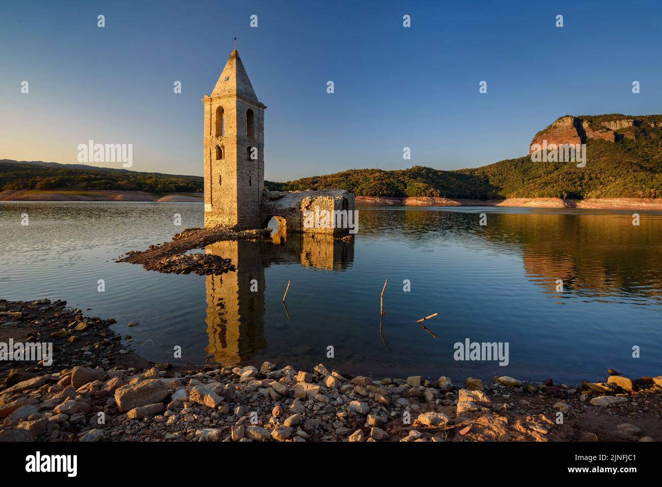 Sonnenaufgang am Glockenturm von Sant Romà de Sau und dem Stausee Sau während der Sommertrockenheit von 2022 (Osona, Barcelona, Katalonien, Spanien) Stockfoto