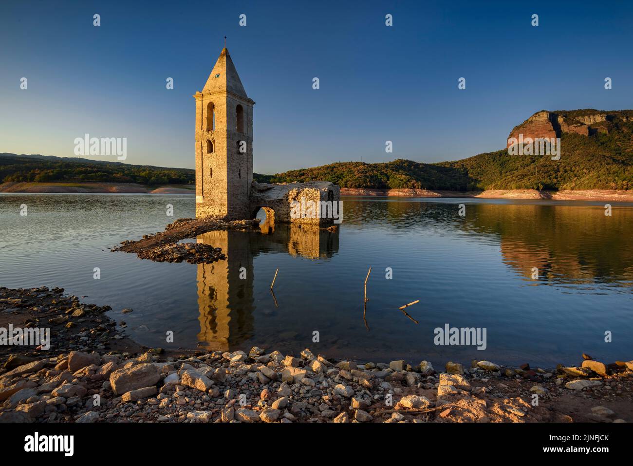 Sonnenaufgang am Glockenturm von Sant Romà de Sau und dem Stausee Sau während der Sommertrockenheit von 2022 (Osona, Barcelona, Katalonien, Spanien) Stockfoto