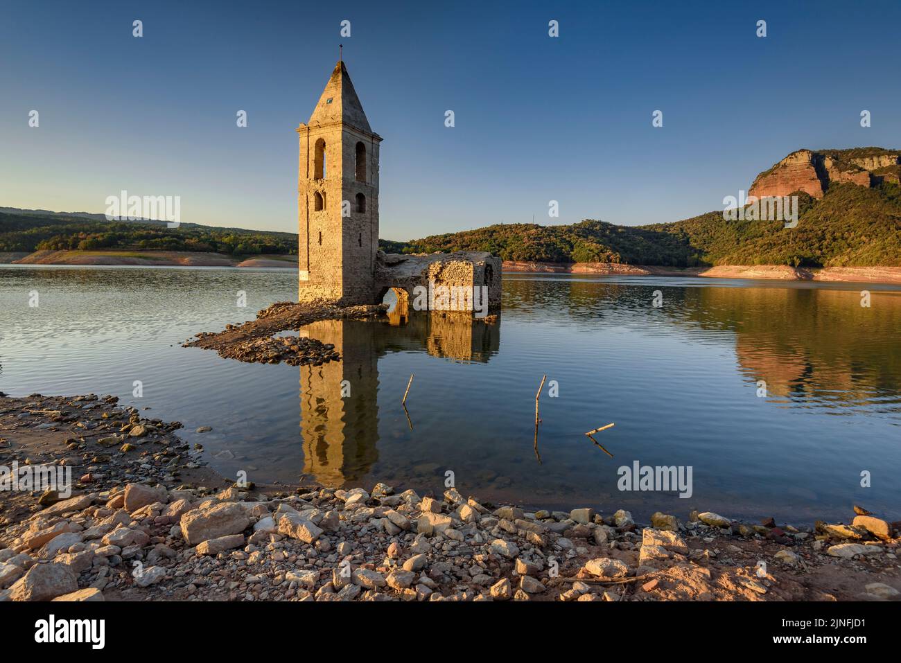 Sonnenaufgang am Glockenturm von Sant Romà de Sau und dem Stausee Sau während der Sommertrockenheit von 2022 (Osona, Barcelona, Katalonien, Spanien) Stockfoto