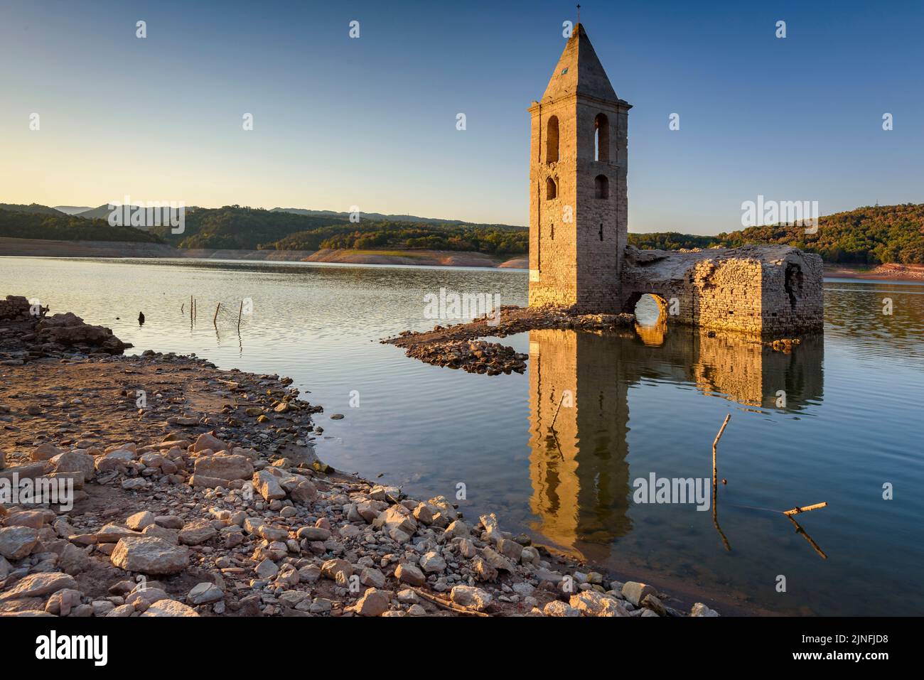 Sonnenaufgang am Glockenturm von Sant Romà de Sau und dem Stausee Sau während der Sommertrockenheit von 2022 (Osona, Barcelona, Katalonien, Spanien) Stockfoto