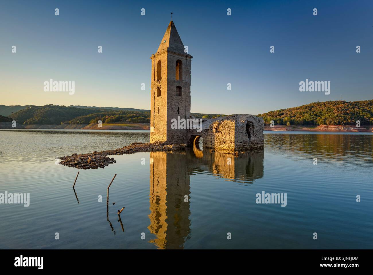 Sonnenaufgang am Glockenturm von Sant Romà de Sau und dem Stausee Sau während der Sommertrockenheit von 2022 (Osona, Barcelona, Katalonien, Spanien) Stockfoto