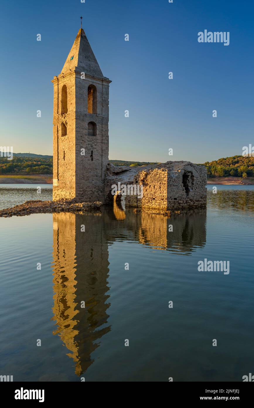 Sonnenaufgang am Glockenturm von Sant Romà de Sau und dem Stausee Sau während der Sommertrockenheit von 2022 (Osona, Barcelona, Katalonien, Spanien) Stockfoto