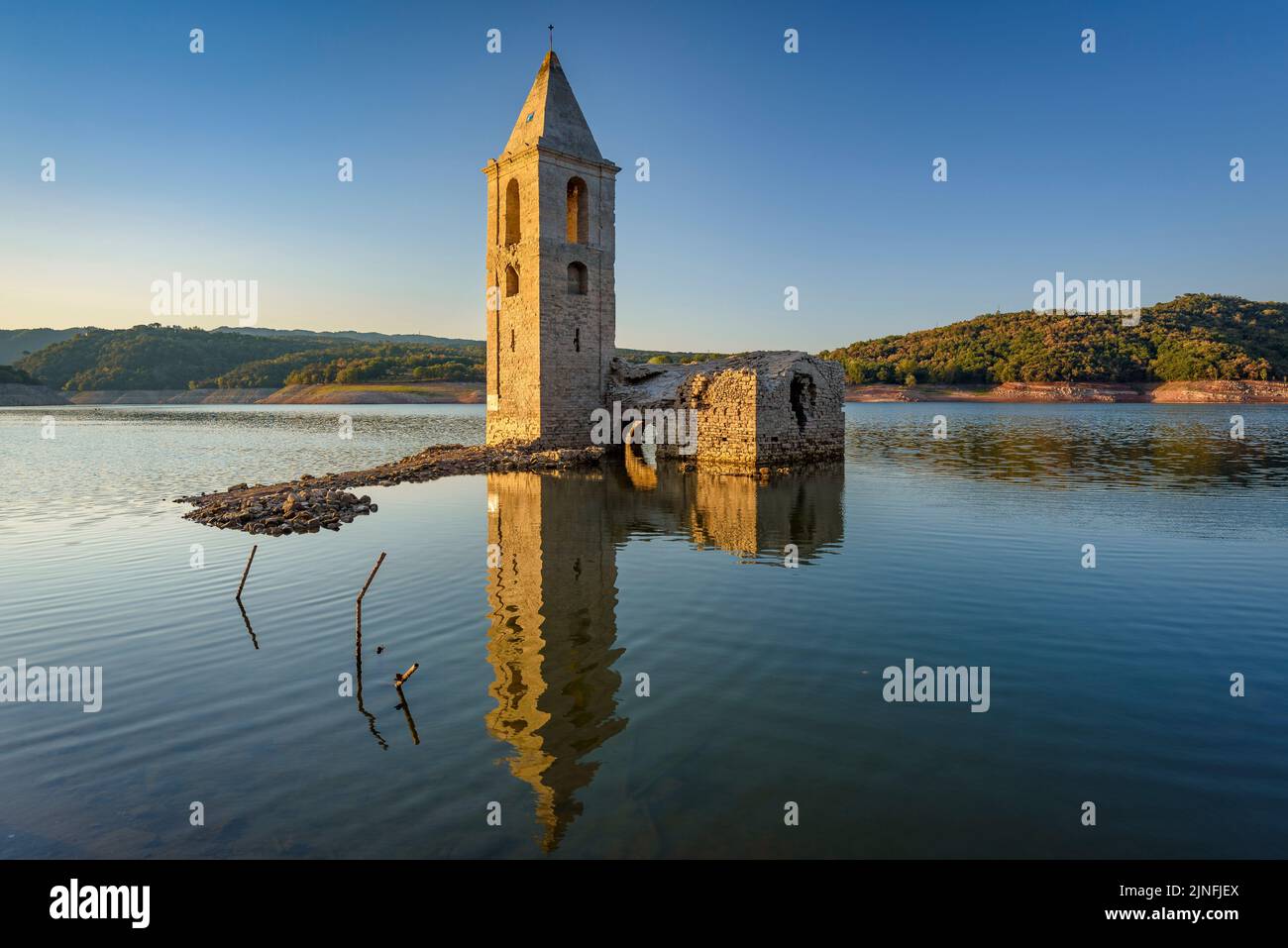 Sonnenaufgang am Glockenturm von Sant Romà de Sau und dem Stausee Sau während der Sommertrockenheit von 2022 (Osona, Barcelona, Katalonien, Spanien) Stockfoto