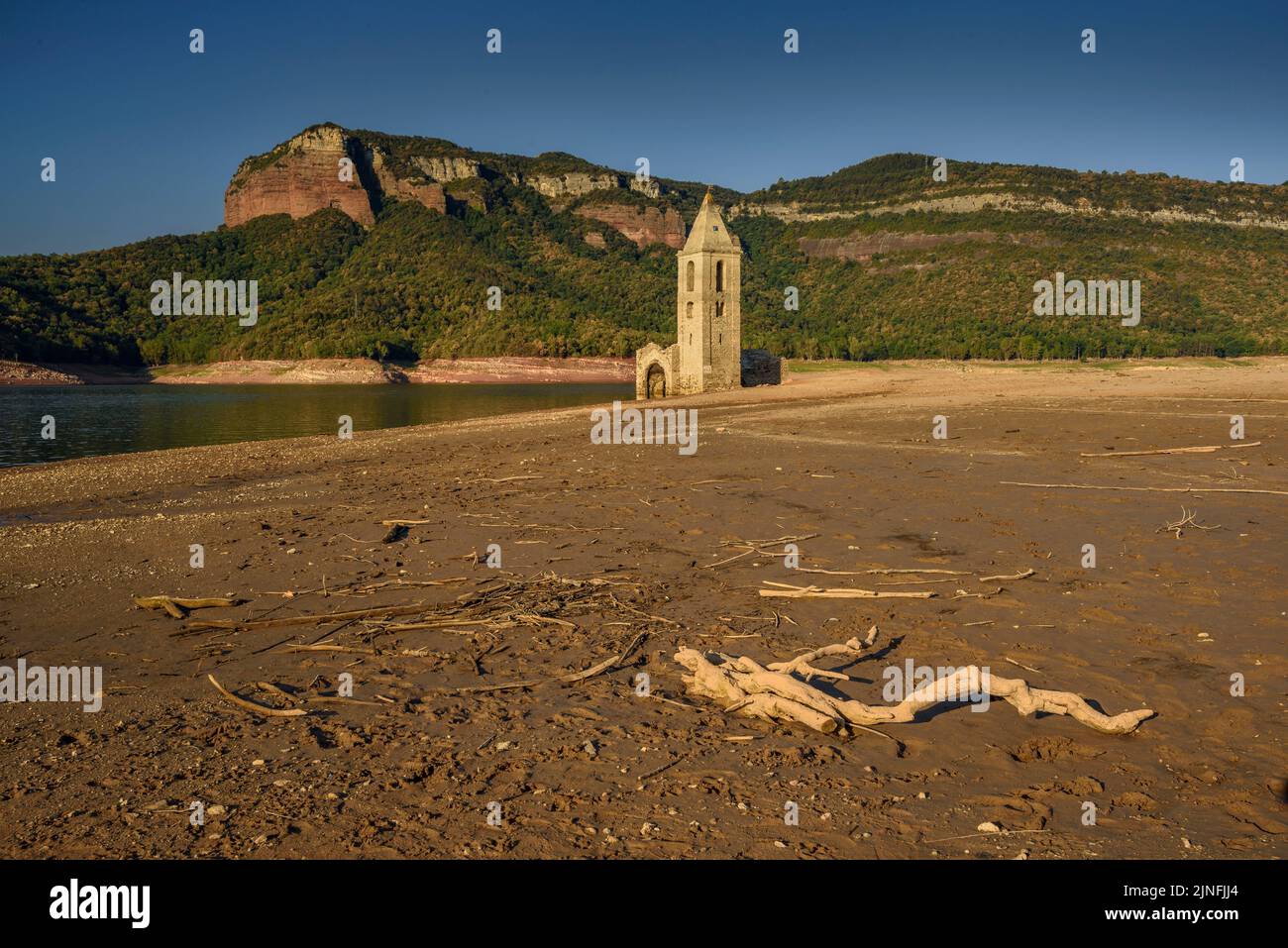Sonnenaufgang am Glockenturm von Sant Romà de Sau und dem Stausee Sau während der Sommertrockenheit von 2022 (Osona, Barcelona, Katalonien, Spanien) Stockfoto
