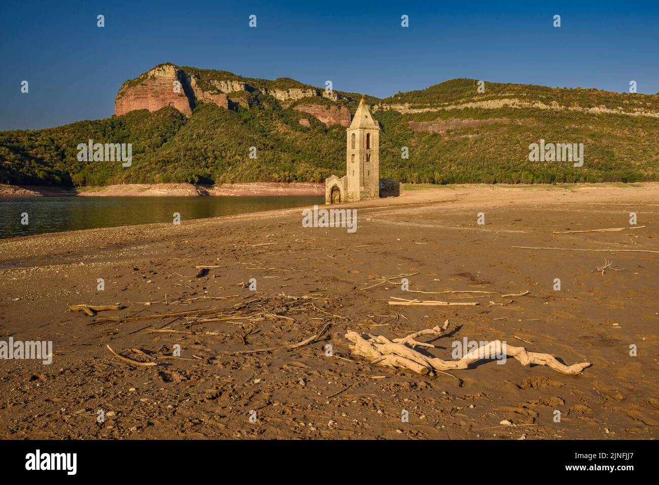 Sonnenaufgang am Glockenturm von Sant Romà de Sau und dem Stausee Sau während der Sommertrockenheit von 2022 (Osona, Barcelona, Katalonien, Spanien) Stockfoto