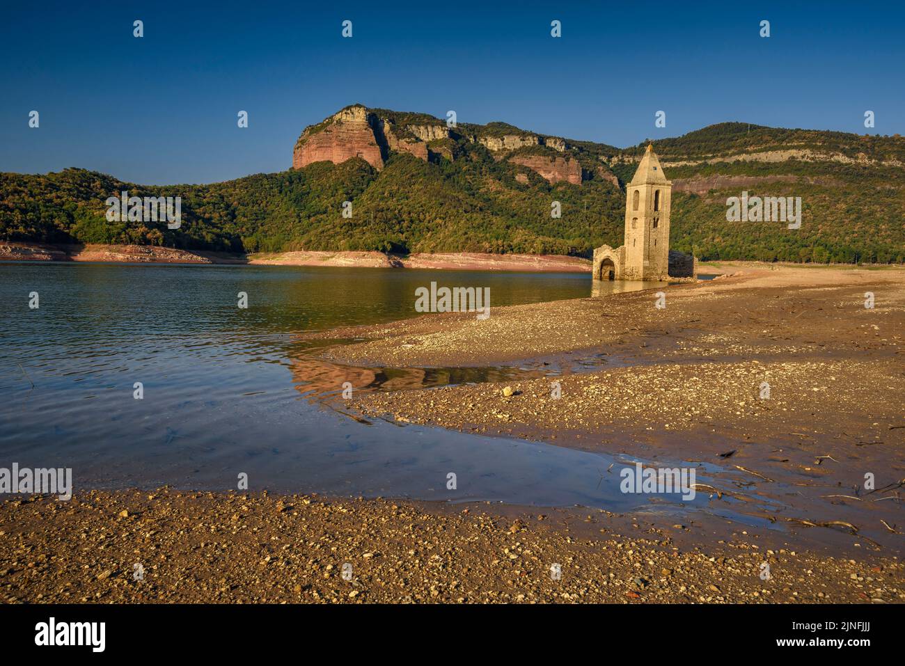 Sonnenaufgang am Glockenturm von Sant Romà de Sau und dem Stausee Sau während der Sommertrockenheit von 2022 (Osona, Barcelona, Katalonien, Spanien) Stockfoto