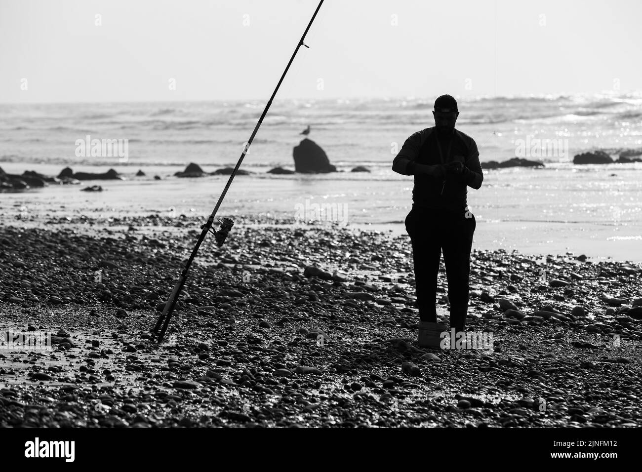 Laayoune, Marokko - 30. Juli 2022 : Ein Fischer und seine Fischerstange in schwarz und weiß Stockfoto