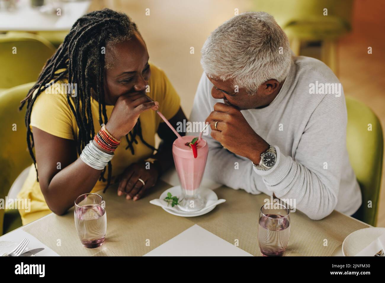 Reifes Paar, das in einem Café einen leckeren Erdbeermilchshake teilt. Sorgenfreies Seniorenpaar, das eine gute Zeit in einem Restaurant hat. Glücklich reifes Paar genießen Stockfoto
