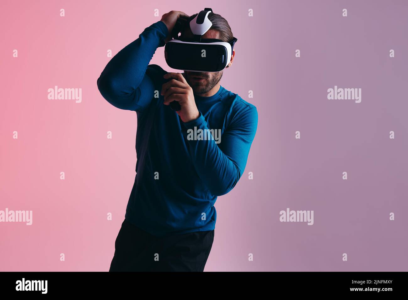 Boxen in der virtuellen Realität. Sportlicher junger Mann, der sich auf einen virtuellen Schlag vorbereitet, während er eine Virtual-Reality-Schutzbrille trägt. Aktiver junger Mann, der virtuelles Re erforscht Stockfoto