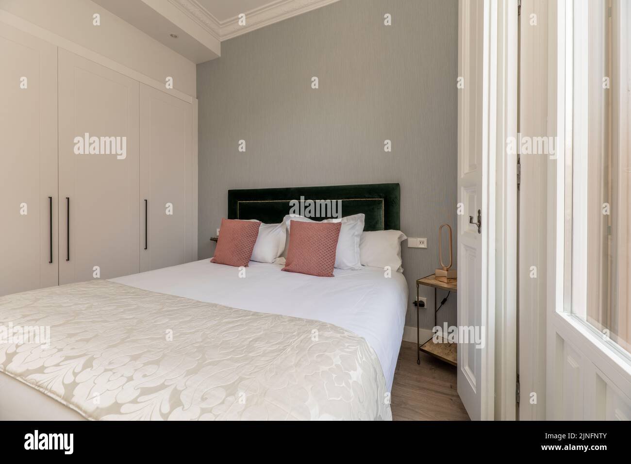 Doppelzimmer mit moderner Dekoration in der Ferienwohnung mit rosa Kissen und eingebautem Kleiderschrank mit weißen Holztüren Stockfoto