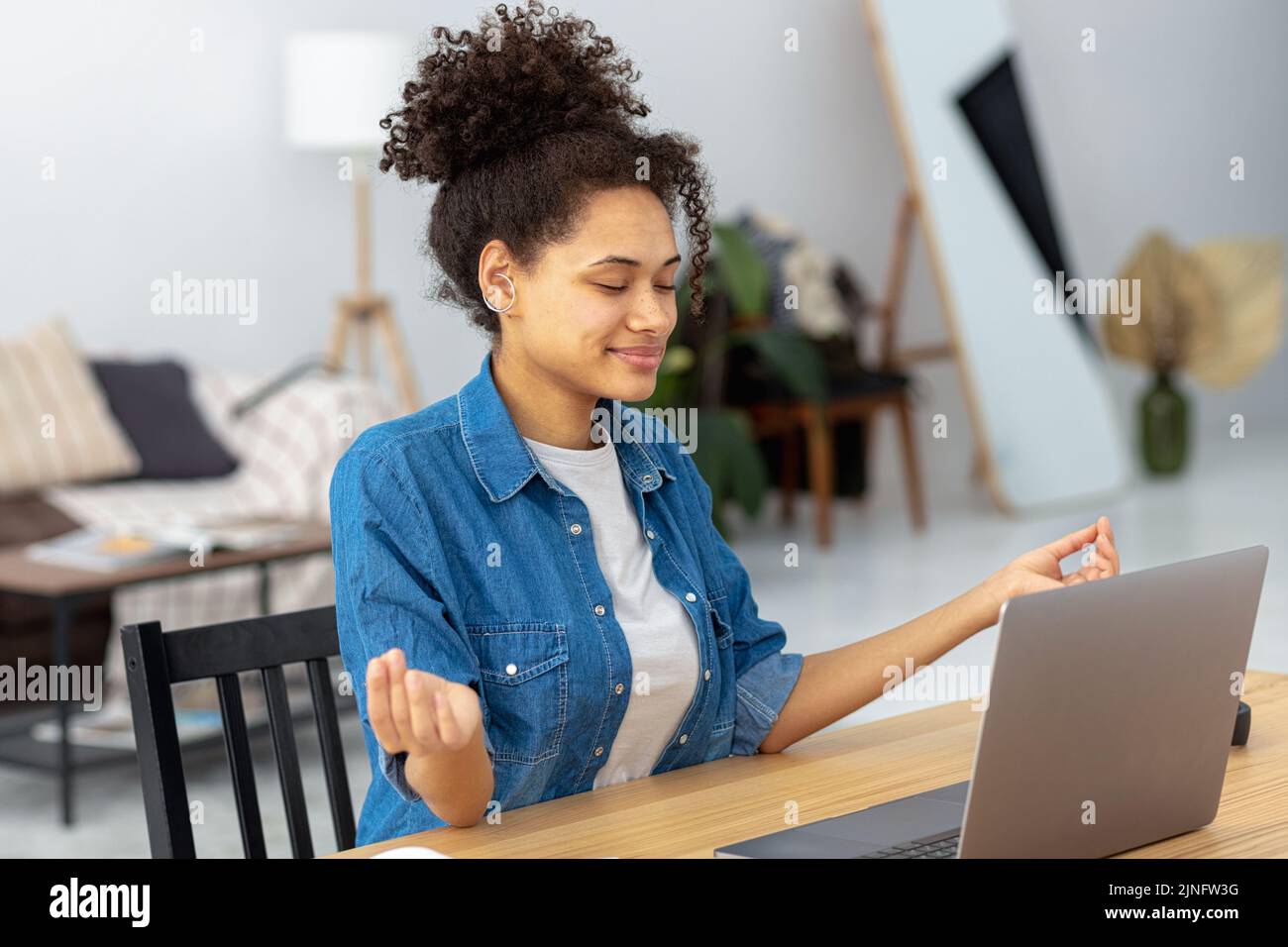 Ruhige afroamerikanische junge Frau, die am Arbeitsplatz im Büro sitzt und meditiert, eine Pause zu machen und stressigen Job zu vermeiden Stockfoto