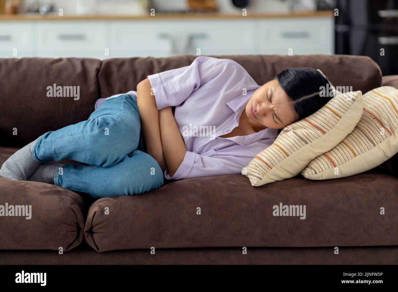 Junge Frau, die zu Hause an Bauchschmerzen leidet und auf der Couch liegt Stockfoto