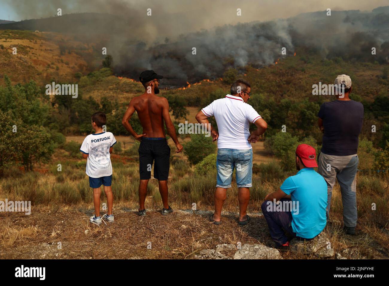 Menschen und ein Kind beobachten ein Lauffeuer in Carrapichana, Celorico da Beira, Portugal, 11. August 2022. REUTERS/Pedro Nunes Stockfoto
