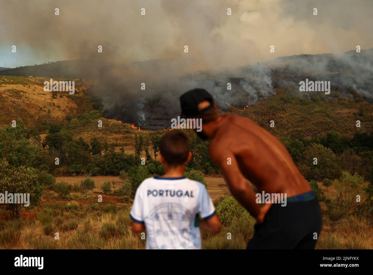 Ein Mann und ein Kind beobachten ein Lauffeuer in Carrapichana, Celorico da Beira, Portugal, 11. August 2022. REUTERS/Pedro Nunes Stockfoto