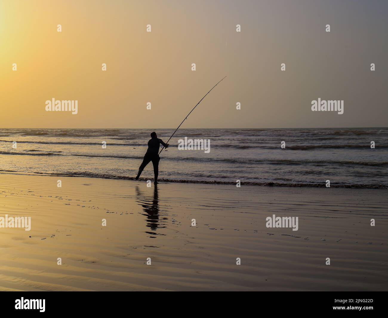 Ein Fischer, der seinen Haken mit seiner Angelrute hält, bei einem wunderschönen Sonnenuntergang in der Stadt Laayoune Stockfoto