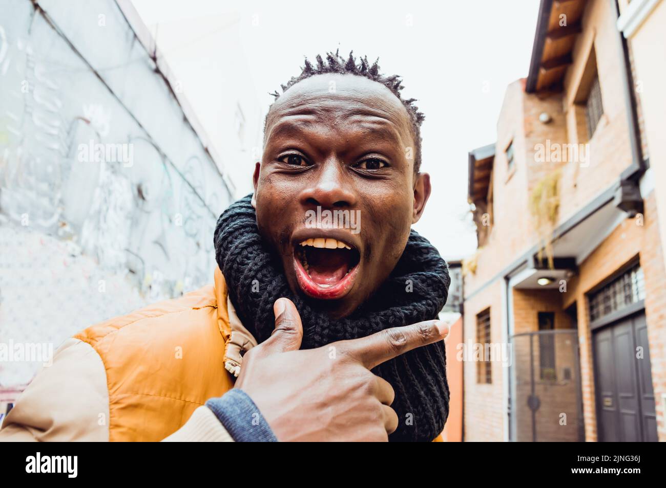 Nahaufnahme eines jungen afrikanischen Mannes, der auf der Straße steht, mit schwarzem Schal, Ausdruck von Freude und mit einem großen Lächeln, der auf die Kamera schaut. Stockfoto