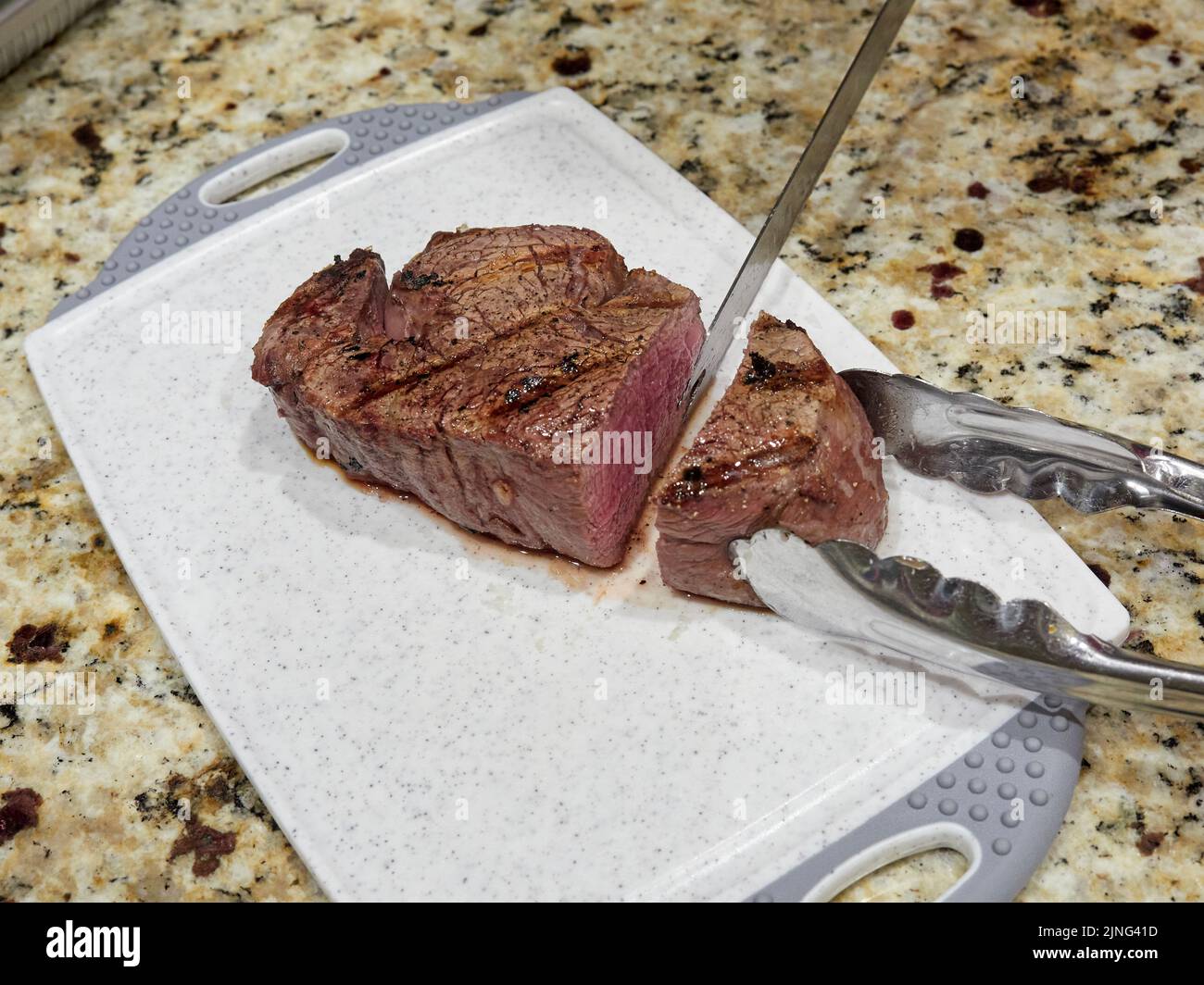 Gegrilltes oder gekochtes mittelseltenes Steak, das für ein Abendessen auf einem Schneidebrett geschnitten wird. Stockfoto