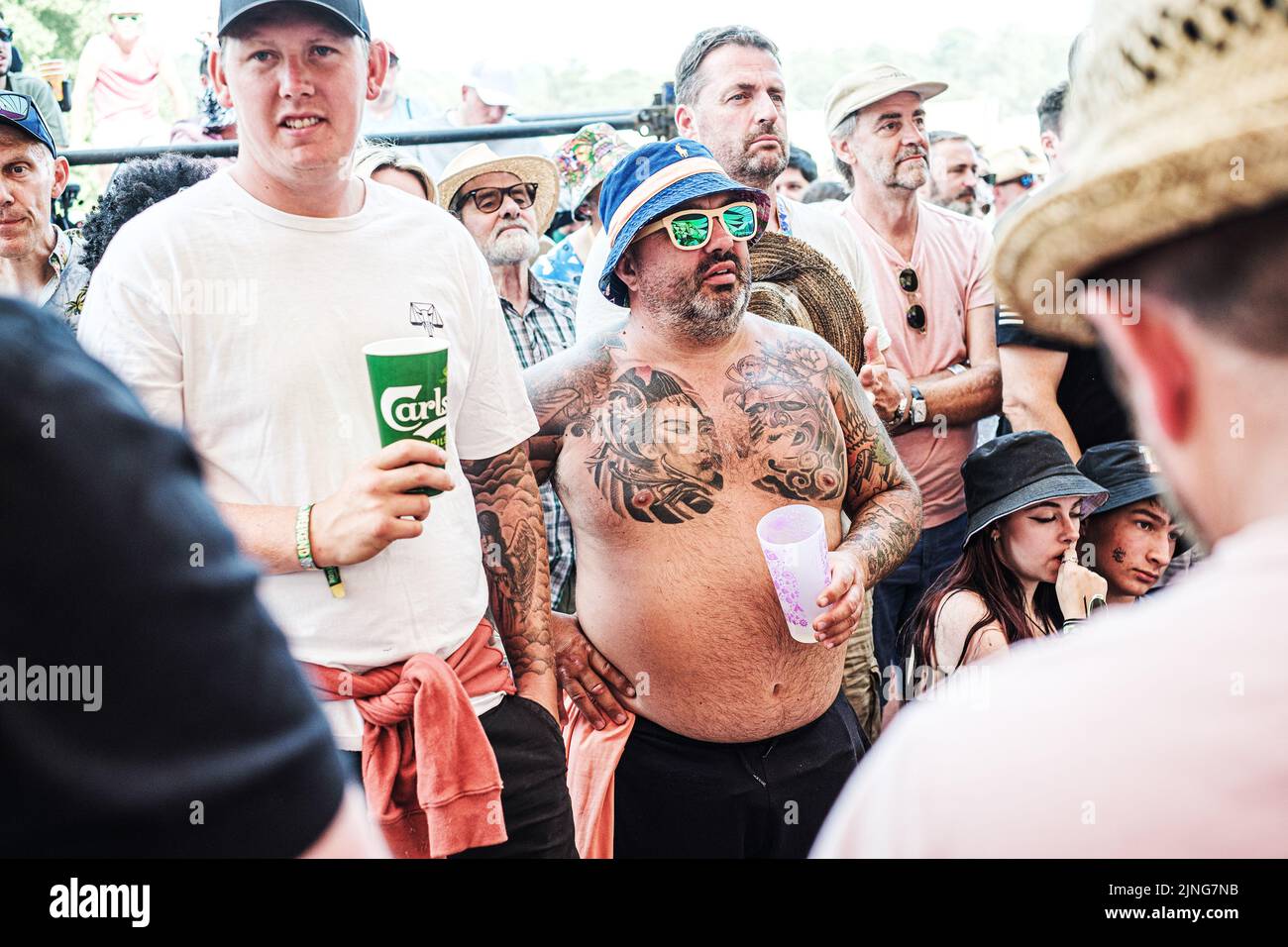 Menschen, die während des Latitude Music Festivals in Suffolk, England, Tassen in der Hand halten, die auf einer Straße stehen Stockfoto