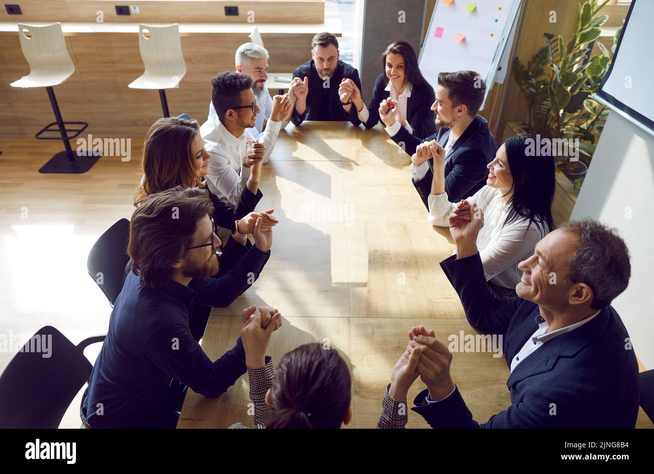 Ein vielseitiges Team glücklicher Geschäftsleute, die am Bürotisch sitzen und die Hände halten Stockfoto